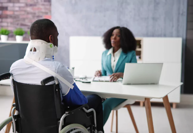 Injured man in wheelchair consulting with provider for disability evaluation.